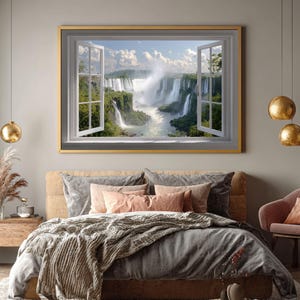 May include: A framed wall art piece depicting a scenic waterfall view through an open window. The artwork is mounted above a bed with gray bedding and peach-colored pillows. Gold pendant lights hang from the ceiling, complementing the artwork's gold frame.