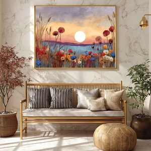 May include: A framed watercolor painting depicts a sunset over a field of colorful wildflowers. The painting is displayed above a gold bench with striped and patterned pillows. A leather ottoman and potted plants complete the scene.