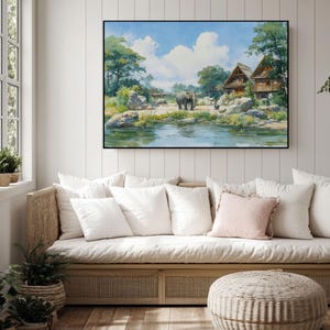 May include: A framed watercolor painting depicts a serene landscape with an elephant and a small calf near a pond. The artwork features a blue sky with fluffy white clouds, lush green trees, and rustic wooden structures. The painting is displayed above a wicker sofa with white pillows.