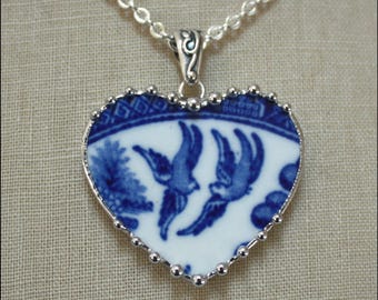 May include: A heart-shaped pendant crafted from a piece of blue and white ceramic featuring a bird pattern, set in a silver-toned metal frame with a beaded edge. The pendant hangs from a silver-toned chain with a decorative scrollwork bail.