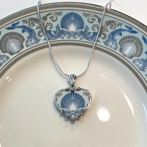 May include: A silver chain necklace with a heart-shaped pendant featuring a blue and white seashell design.