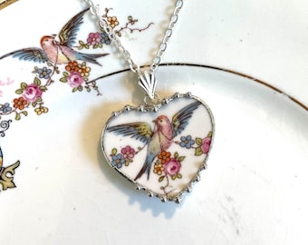 Könnte beinhalten: Eine silberne Kettenkette mit einem herzförmigen Anhänger mit einem Vintage-Porzellanvogel und einem Blumendesign.