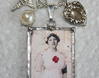 Könnte beinhalten: Eine silberne Halskette mit einem Glasanhänger, der ein Vintage-Bild einer Krankenschwester zeigt, die eine weiße Uniform mit einem roten Kreuz trägt. Der Anhänger hat einen silbernen Rahmen und das Wort "nurse" ist unter dem Bild gedruckt. Die Halskette enthält außerdem einen silbernen Herzanhänger, eine Perle und einen Anhänger mit einem medizinischen Symbol.