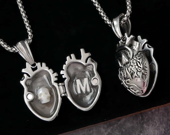 Puede incluir: Collares con colgantes plateados en forma de corazón. Uno de los colgantes se abre para revelar una pequeña calavera, el otro muestra la letra "M". El tercero es un corazón anatómico detallado. Los tres cuelgan de una cadena plateada.