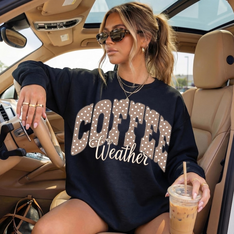 May include: Black sweatshirt with the words "COFFEE Weather" in a brown polka dot design. The sweatshirt is worn by a person in a car, holding a coffee drink.