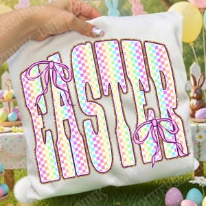 May include: White cushion featuring the word "EASTER" in large, colourful checkered letters outlined in gold glitter. Pink bows decorate the letters. The cushion is held up by a person.