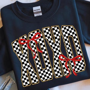 Puede incluir: Sudadera negra con la palabra "XOXO" en un patr&oacute;n de cuadros blanco y negro, con ribete de purpurina dorada y lazos rojos. Una prenda informal.