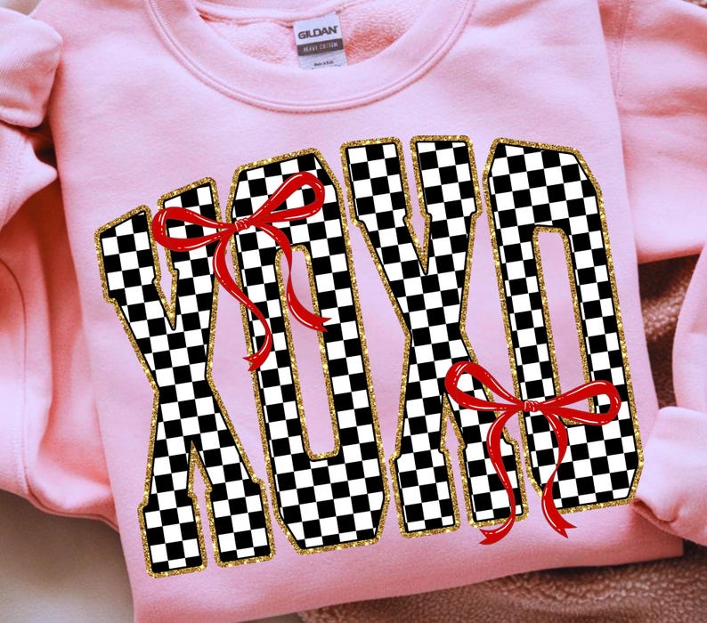 Puede incluir: Una sudadera rosa claro con las letras "XOXO" en un patr&oacute;n de cuadros blancos y negros. Las letras est&aacute;n delineadas con purpurina dorada y adornadas con lazos rojos. La sudadera tiene cuello redondo y mangas largas.