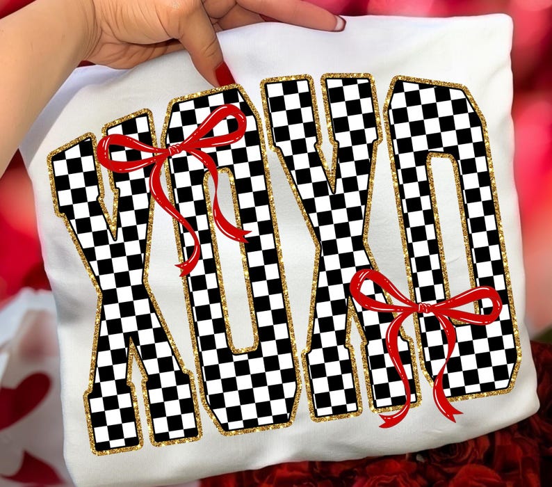 Puede incluir: Camiseta blanca con las letras XOXO en un patr&oacute;n de cuadros blanco y negro, delineadas con purpurina dorada. Lazos rojos est&aacute;n unidos a las letras. La camiseta es sostenida por una mano.
