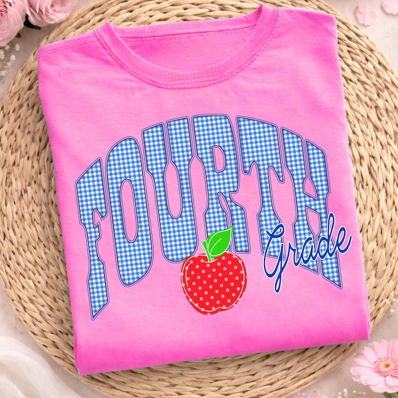 May include: A pink t-shirt with the words "FOURTH Grade" in a blue gingham pattern and script. A red apple with white polka dots and a green leaf is below the text. The shirt is made of a soft material.