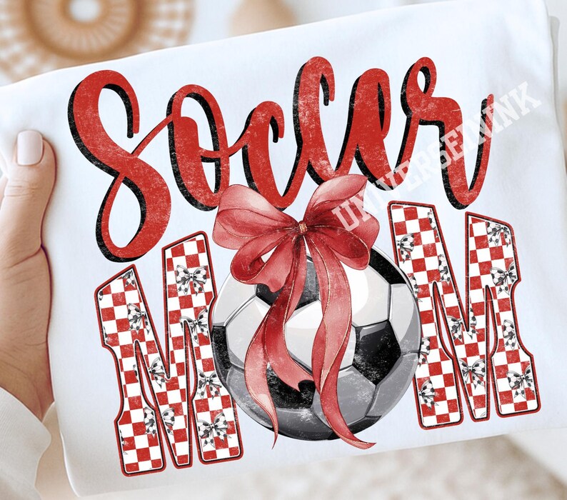 May include: White t-shirt with the words "Soccer Mom" in red script and checkered letters. A soccer ball with a red bow is in the center. The design is a festive, sporty theme.