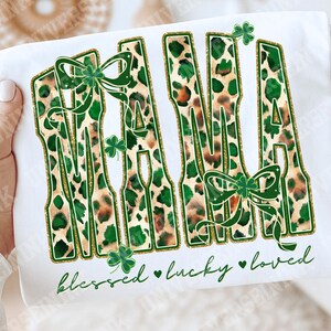 May include: White t-shirt featuring the word "MAMA" in a green and brown leopard print design, accented with green bows and shamrocks. The words "blessed, lucky, loved" are written in green script below the word "MAMA".