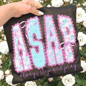 May include: Black pillow with the letters "ASAP" in a floral and polka dot design, outlined in pink lace. The letters are accented with pink bows. The phrase "always stop and pray" is written in cursive below the letters.