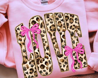 May include: Pink sweatshirt with the word "LOVE" in a leopard print design outlined in gold. The letters are adorned with pink bows. The sweatshirt is a soft, comfortable material.