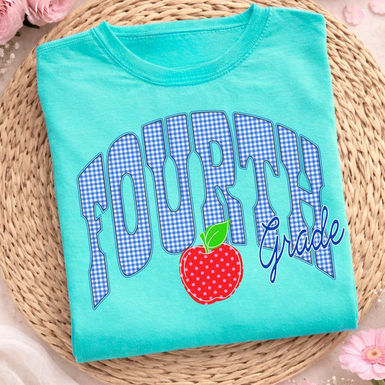 May include: A turquoise t-shirt with the words "FOURTH Grade" in a blue gingham pattern. A red apple with white polka dots and a green leaf is below the text. The shirt is folded on a woven mat.