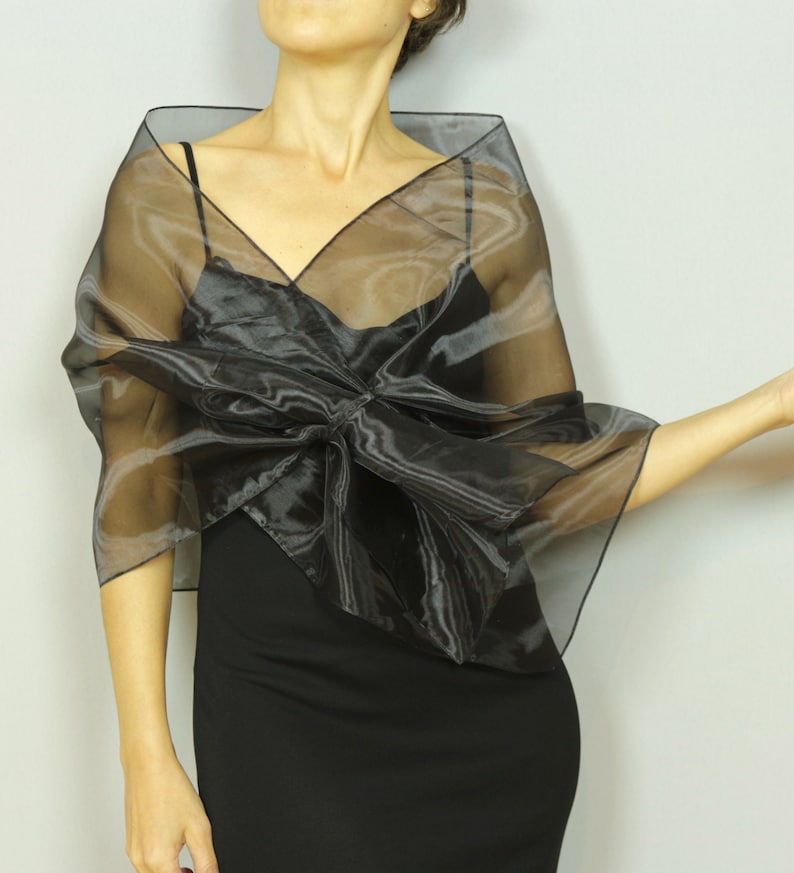 May include: A black sheer shawl with a large bow in the front. The shawl is made of a lightweight, flowing fabric and is perfect for adding a touch of elegance to any outfit.