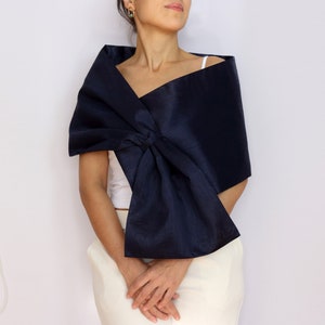 Pu&ograve; includere: Uno scialle blu navy con un grande dettaglio a nodo. Lo scialle &egrave; drappeggiato sulle spalle. Il tessuto ha una leggera lucentezza. La persona indossa un top bianco e pantaloni color crema.