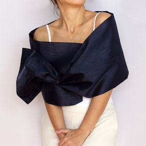 Pu&ograve; includere: Uno scialle blu navy con un grande fiocco. Lo scialle &egrave; drappeggiato sulle spalle e annodato sul davanti. La modella indossa una canotta bianca e pantaloni color crema.