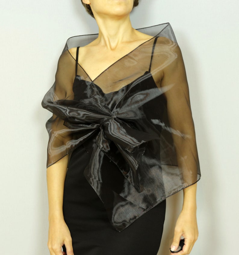 May include: A black sheer shawl with a large bow in the front. The shawl is made of a lightweight, flowing fabric.