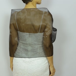 May include: A black sheer shawl with a ruffled edge. The shawl is draped over the shoulders of a person wearing a white lace dress.