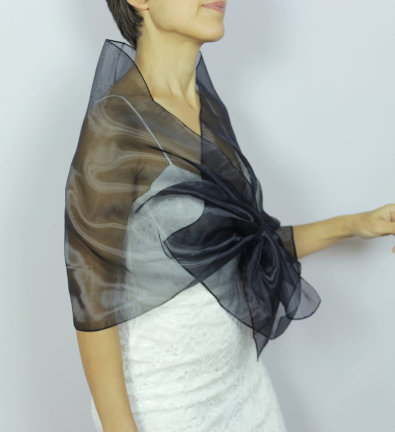 May include: A black sheer shawl with a large bow tied in the front. The shawl is made of a lightweight, flowing fabric and is perfect for adding a touch of elegance to any outfit.
