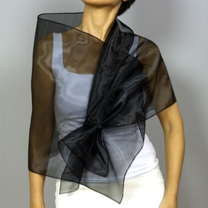 May include: A black sheer shawl with a large bow in the front. The shawl is draped over a white tank top.