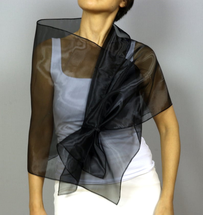 May include: A black sheer shawl with a large bow in the front. The shawl is draped over a white tank top.