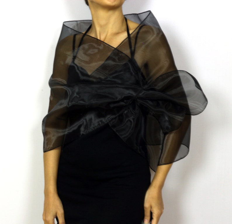 May include: A black sheer shawl with a large bow in the front. The shawl is made of a lightweight, flowing fabric.