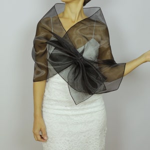 May include: A black sheer shawl with a large bow in the front. The shawl is draped over a white lace dress.