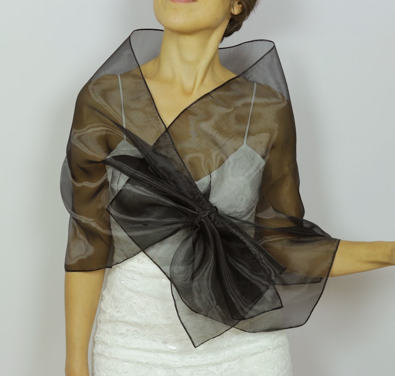 May include: A black sheer shawl with a large bow in the front. The shawl is made of a lightweight fabric and is perfect for adding a touch of elegance to any outfit.