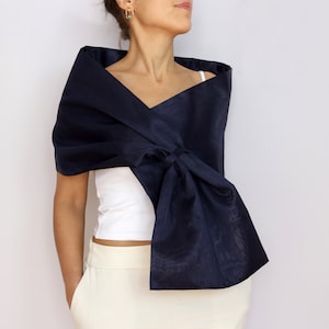 Pu&ograve; includere: Uno scialle blu navy drappeggiato sulle spalle, annodato sul davanti. Lo scialle &egrave; realizzato in un tessuto lucido e viene indossato sopra un top bianco e pantaloni color crema. L'aspetto generale &egrave; elegante e sofisticato.