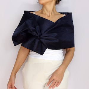 Pu&ograve; includere: Uno scialle blu navy con un grande fiocco. Lo scialle &egrave; indossato sopra un top bianco e pantaloni color crema. Il tessuto ha una lucentezza sottile. L'aspetto generale &egrave; elegante e sofisticato.