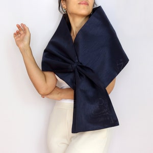 Pu&ograve; includere: Uno scialle blu navy con un grande fiocco. Il tessuto lucido &egrave; drappeggiato sulle spalle. Lo sfondo &egrave; bianco.