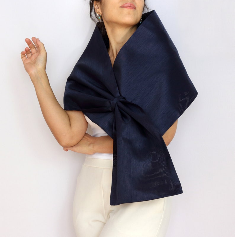 Pu&ograve; includere: Uno scialle blu navy con un grande fiocco. Il tessuto lucido &egrave; drappeggiato sulle spalle. Lo sfondo &egrave; bianco.
