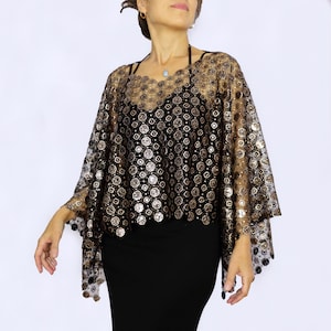 Puede incluir: Un poncho de encaje negro transparente con lentejuelas doradas en forma de círculo. El poncho tiene un dobladillo festoneado y se lleva sobre un vestido negro.