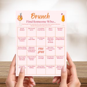May include: A pink brunch game card with the text "Brunch Find Someone Who..." and various prompts. The card is held by hands and features cocktail illustrations. The game is designed for a social gathering.