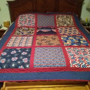 May include: A patchwork quilt with a patriotic theme, featuring squares of red, white, and blue fabrics. The quilt showcases various patterns, including American flags, stars, and stripes, with a red border and a blue dotted edge.