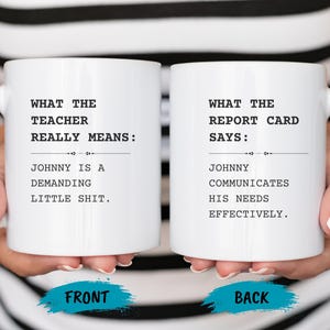 May include: Two white ceramic mugs with black text. One mug reads "WHAT THE TEACHER REALLY MEANS: JOHNNY IS A DEMANDING LITTLE SHIT." The other mug says "WHAT THE REPORT CARD SAYS: JOHNNY COMMUNICATES HIS NEEDS EFFECTIVELY."