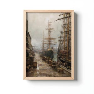 Puede incluir: Una impresión enmarcada de una escena portuaria con altos barcos atracados a lo largo de un muelle de madera. La obra de arte presenta tonos apagados de marrón, gris y azul, con un cielo nublado. La impresión está en un marco de madera clara.