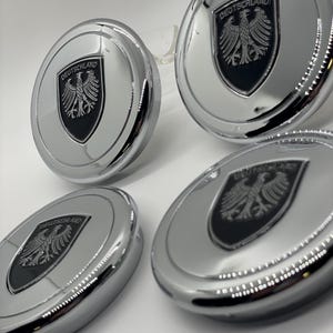 May include: Four silver car hubcaps with a black and silver German eagle emblem and the word "DEUTSCHLAND" in black lettering.