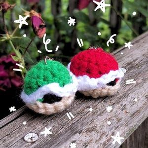 May include: A pair of handmade crochet earrings. One earring is green, the other is red, both with white trim and a tan base. The earrings are round and have a festive appearance, possibly holiday-themed. They are displayed on a weathered wooden surface.