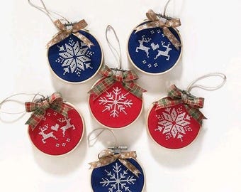 Könnte beinhalten: Sechs runde Weihnachtskugeln mit gestickten Designs. Die Ornamente haben Holzreifen und Schleifen. Die Designs zeigen Schneeflocken und Rentiere in Rot und Blau.
