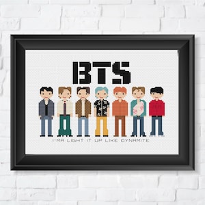May include: A black framed cross-stitch pattern featuring a group of seven cartoon figures with the word "BTS" above them and the text "I'm a light it up like dynamite" below them.