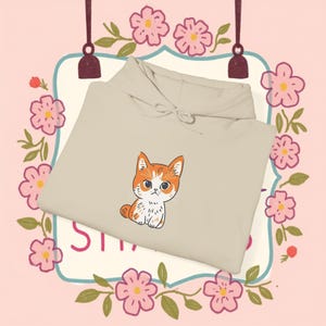 May include: A beige hoodie featuring a cute orange and white kitten illustration. The kitten is sitting with its paws tucked under its body and looking at the viewer.