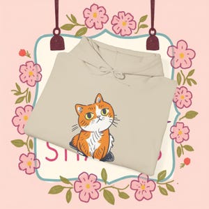 May include: A beige hoodie featuring a cartoon illustration of an orange tabby cat. The cat is looking to the right and has a white chest and paws.