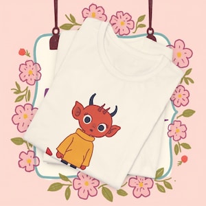 May include: White t-shirt with a red cartoon devil wearing a yellow sweater. The devil has horns and a surprised expression.