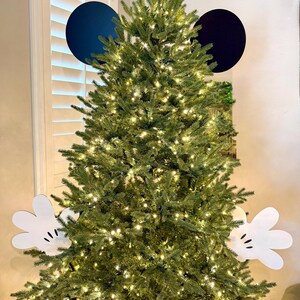 May include: A decorated Christmas tree with white Mickey Mouse gloves and two large navy blue circles for ears. The tree is lit with small white lights, creating a festive holiday display.