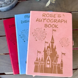 K&ouml;nnte beinhalten: Drei rechteckige Autogrammb&uuml;cher in Pink, Blau und Rot. Das pinke Buch zeigt ein Schlossmotiv, Feuerwerk und den Text "ROSE'S AUTOGRAPH BOOK". Die blauen und roten B&uuml;cher zeigen teilweise den Text "DISNEY" und "AUTOGRAPH BOOK" mit Feuerwerksmotiven.