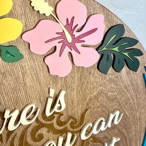May include: Wooden round sign with a light brown finish, featuring a pink hibiscus flower, yellow flower, and green leaves. The sign has the text "There is you can won't" in white script, with a blue border.