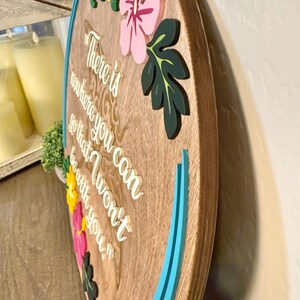 May include: Wooden round sign with a light brown finish, featuring the quote "There is nowhere you can go that I won't be with you." Adorned with colorful flowers in pink, yellow, and green, and a turquoise border. A decorative piece for home decor.
